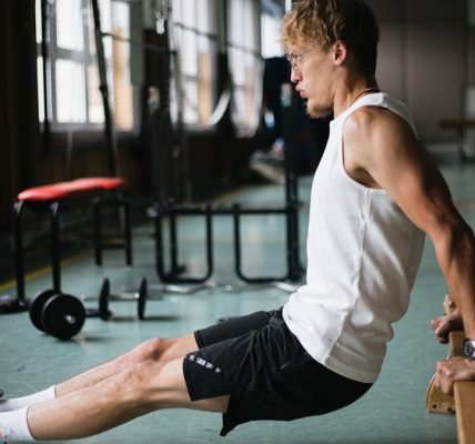 Side view of muscular sportsman in sportswear and glasses doing tricep dips exercises in gym