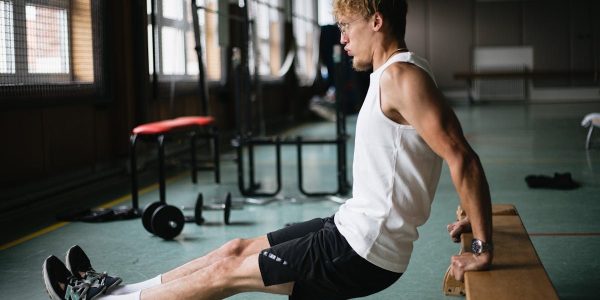 Side view of muscular sportsman in sportswear and glasses doing tricep dips exercises in gym